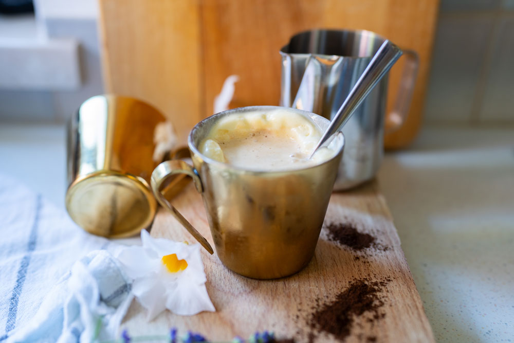 Ein Becher mit Affogato al Caffee sowie einigen Milchkannen im Hintergrund