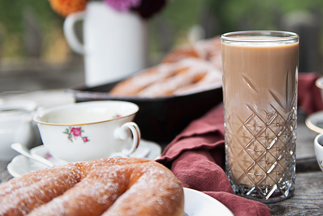 Ein Tisch, gedeckt mit Almkaffee im Glas und Krapfen, sowie Dekoration im Hintergrund