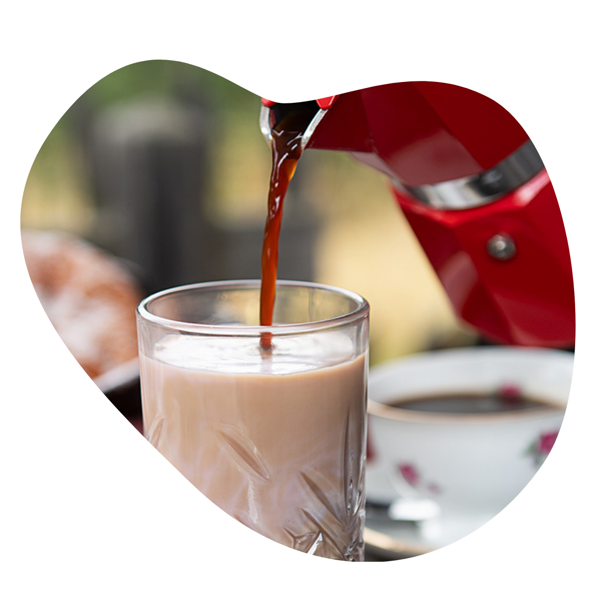 Kaffee wird aus einer Mokakanne in ein Glas gegossen, im Glas befindet sich Milchkaffee