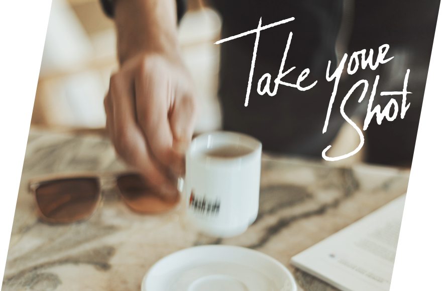 eine hand nimmt eine Tasse Segafredo Kaffee, daneben liegen am Tisch Sonnenbrille und Papier. Die Aufnahme ist verschwommen. Darüber appliziert ist der Schriftzug 