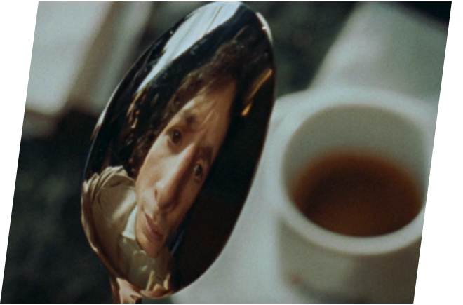 Ein Mann reflektiert sich im Rücken eines Löffles, darunter steht eine volle Kaffeetasse